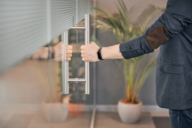 Camdan yansıyan arka planı olan bir adam kapıyı açar.