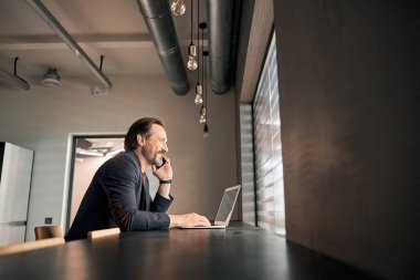 Neşeli gülümseyen adam yeni kitabın üzerinde çalışıyor ve cep telefonuyla sohbet ediyor.
