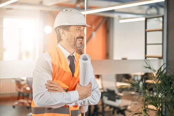 Веселий чоловік у білому шоломі та помаранчевій формі в офісі — стокове фото