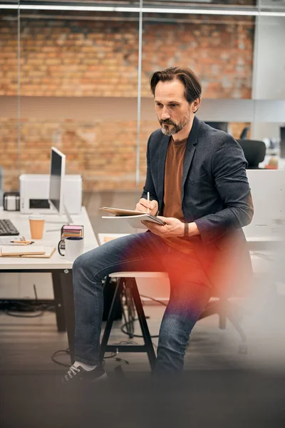 Mann in braunem Hemd und Jeans sitzt im Büro auf dem Tisch — Stockfoto