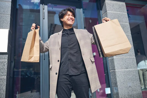 Radosny młody człowiek stojący na ulicy po udanych zakupach — Zdjęcie stockowe