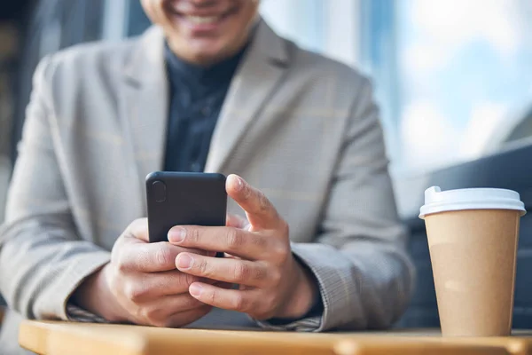 Joven sonriente usando un teléfono inteligente moderno en la cafetería al aire libre —  Fotos de Stock