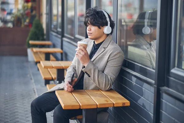Guapo joven en los auriculares beber café en la cafetería al aire libre —  Fotos de Stock