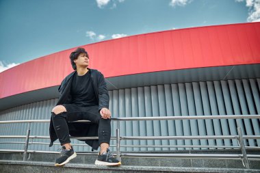 Şık bir genç adam metal korkuluklarda oturuyor.