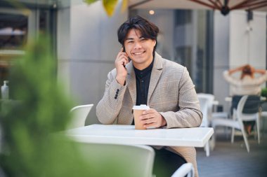 Açık kafede cep telefonuyla konuşan neşeli genç adam.