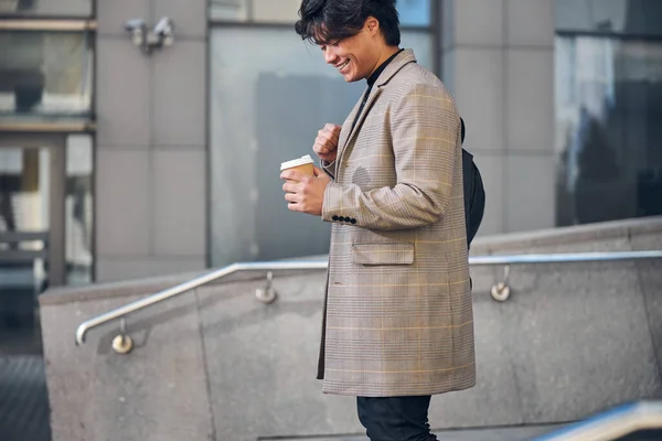Fröhlicher Kerl mit Heißgetränk steht auf der Straße — Stockfoto