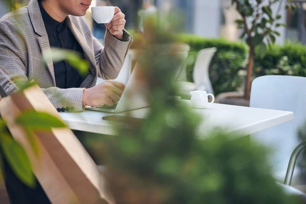 Junger Mann benutzt Notebook und trinkt Kaffee in Café im Freien — Stockfoto