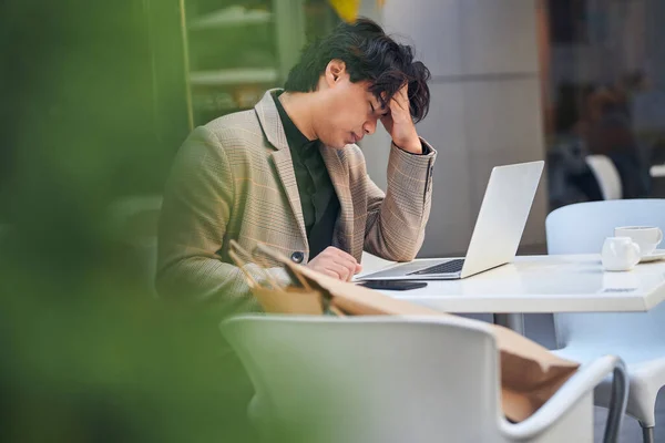 Homem exausto trabalhando em notebook no café ao ar livre — Fotografia de Stock