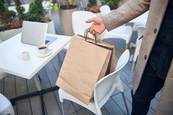 Młody człowiek chwytając torby na zakupy w kawiarni na świeżym powietrzu — Zdjęcie stockowe