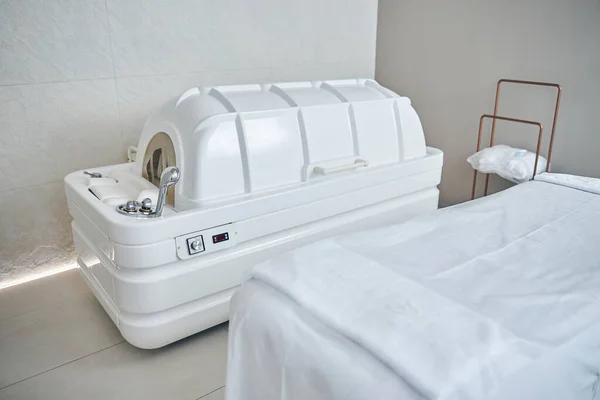 Modern spa capsule and spacious medical couch next to it