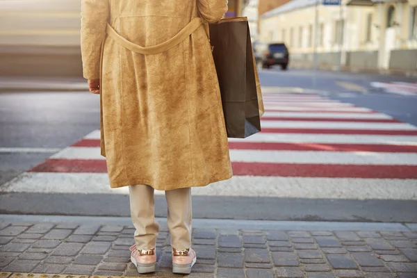 Visão traseira da mulher idosa em casaco marrom com sacos de corte na mão — Fotografia de Stock