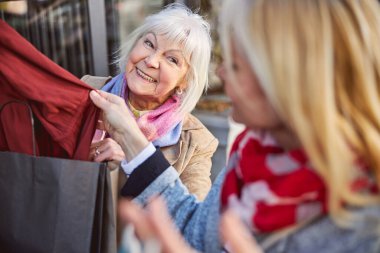 Olgun kadın, bayan arkadaşlarına kırmızı elbiseler gösteriyor.