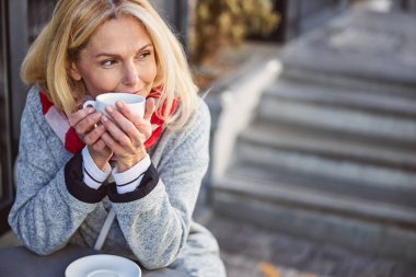 Güzel görünüşlü, gülümseyen bayan sıcak içeceği dışarıda tutuyor.
