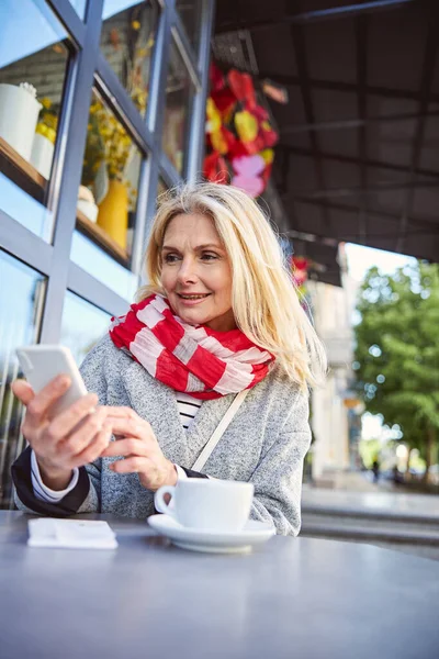 Lächelnde hübsche Frau, die auf den Bildschirm ihres Smartphones blickt — Stockfoto