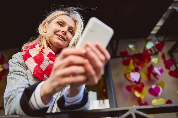 Volwassen vrouw dragen rode sjaal buiten terwijl op zoek naar de telefoon scherm — Stockfoto