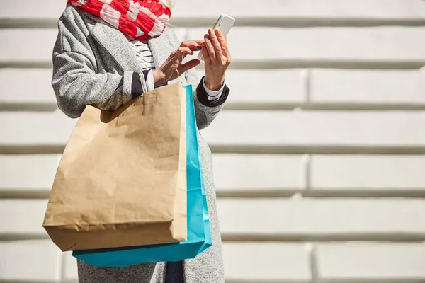 Feminino segurando pacotes de papel na mão ao usar o smartphone — Fotografia de Stock