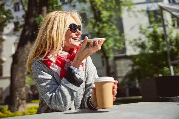Улыбающаяся женщина в повседневной одежде и солнечных очках с современным смартфоном в руке — стоковое фото