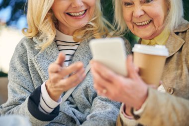 Yetişkin bir kadın ve kız arkadaşı ekrandaki cep telefonuna bakıyor.