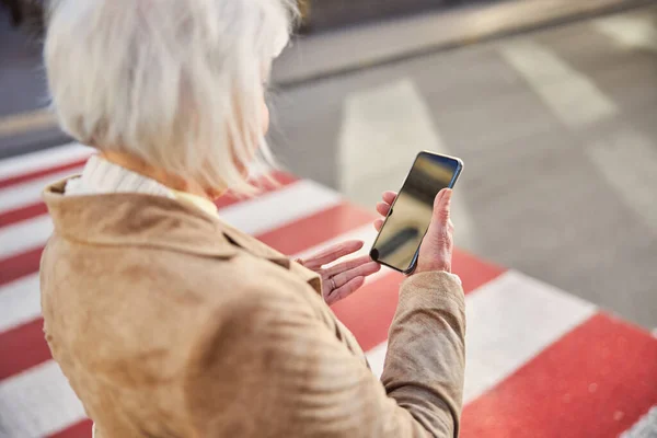 Portré gyönyörű nyugdíjas nő a városban, miközben nézi a fekete képernyőn a telefon — Stock Fotó