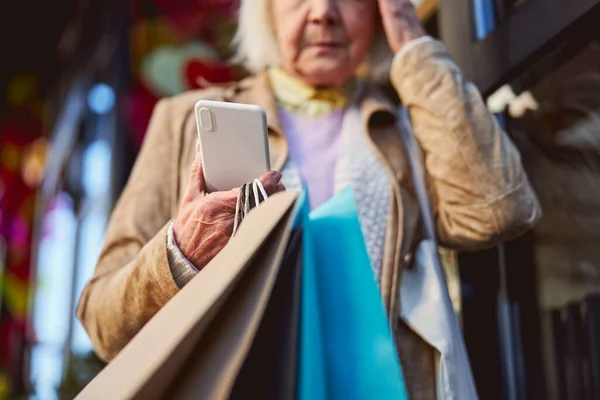 Szomorú idős nő áll az utcán, miközben várja a hívást az okostelefonján — Stock Fotó