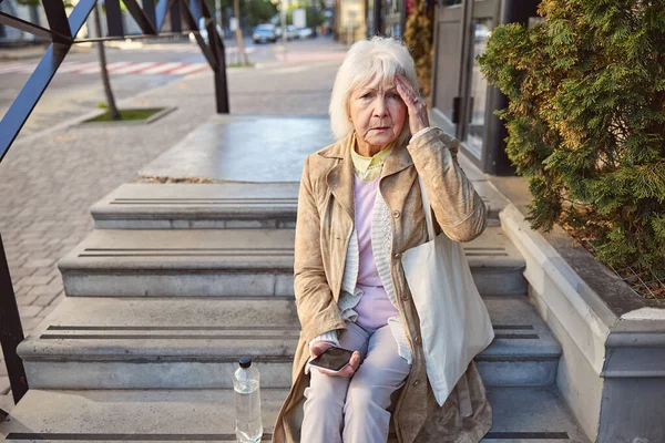 Грустная женщина с бутылкой воды сидит на ступеньках возле здания — стоковое фото