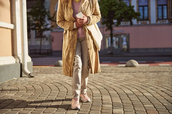 Äldre kvinna bär brun rock och håller mobiltelefon i händerna — Stockfoto