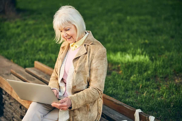 Karcsú idős nő szőke hajjal ül a padon egy parkban — Stock Fotó