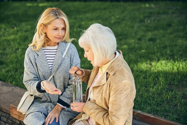 Mature lady feeling ill near female friend in the park — Stock Photo, Image