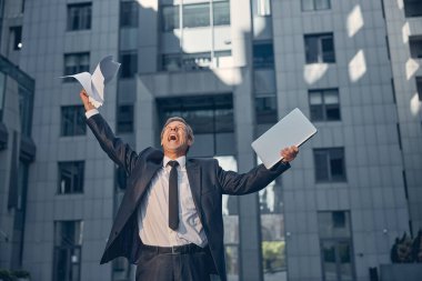 Bilgisayarlı mutlu iş adamı sokaklarda seviniyor.