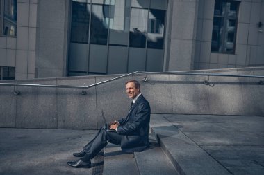 Neşeli iş adamı sokakta modern laptop kullanıyor.