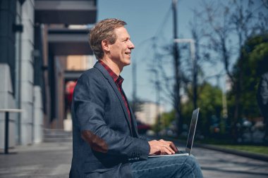 Sokakta dizüstü bilgisayarda çalışan yakışıklı bir adam.