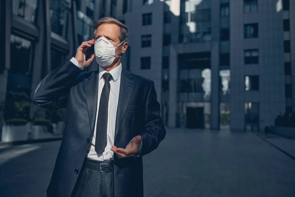 Homem bonito no respirador antiviral falando no celular ao ar livre — Fotografia de Stock