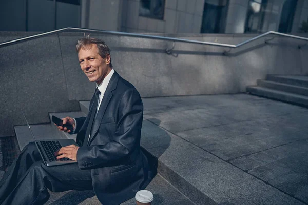 Glada man i kostym med bärbar dator och mobiltelefon på gatan — Stockfoto