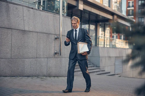 Knappe zakenman die op straat loopt en een mobieltje gebruikt — Stockfoto