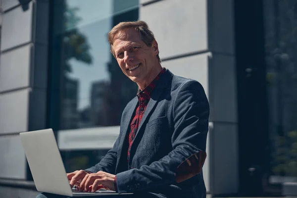 Homem alegre trabalhando em laptop moderno ao ar livre — Fotografia de Stock