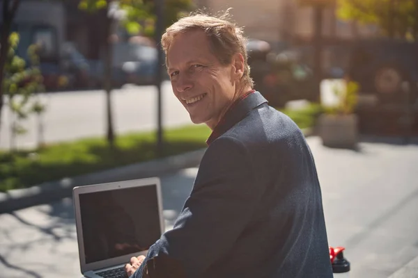 Fröhlicher Mann mit Laptop an sonnigem Tag in der Stadt — Stockfoto