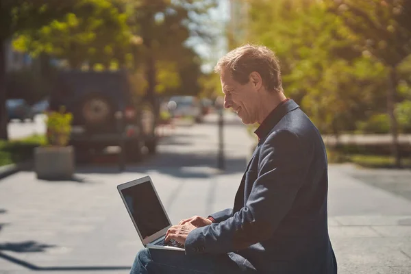Веселий чоловік працює на ноутбуці в сонячний день — стокове фото