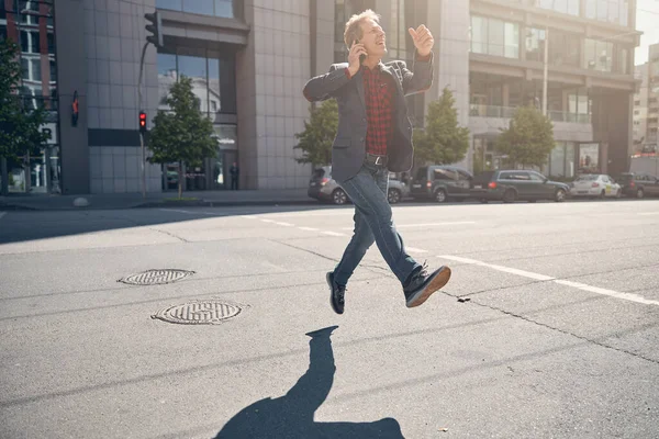 Счастливый человек разговаривает по мобильному телефону во время ходьбы и прыжки на улице — стоковое фото