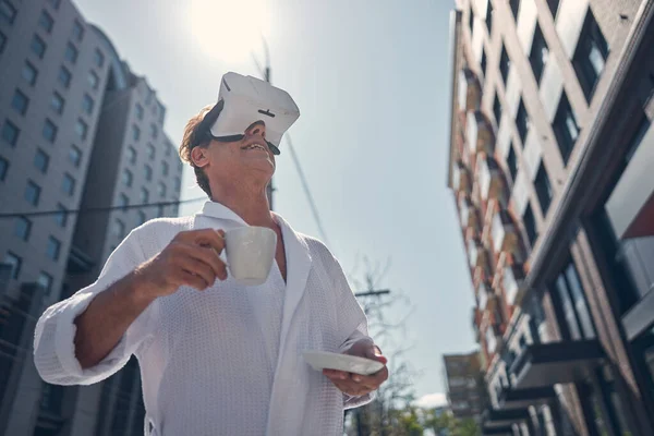 Joyful man in bathrobe using VR headset outdoors