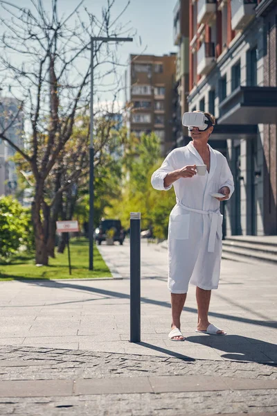 Uomo sorridente in accappatoio utilizzando VR auricolare all'aperto — Foto Stock