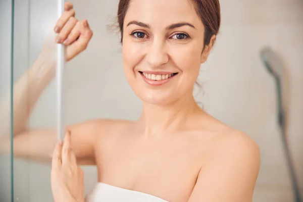 Femme brune souriante appuyée contre une porte de douche coulissante — Photo