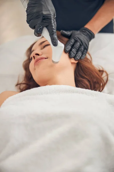 Esteticista en guantes negros reduciendo las arrugas en la barbilla del cliente — Foto de Stock