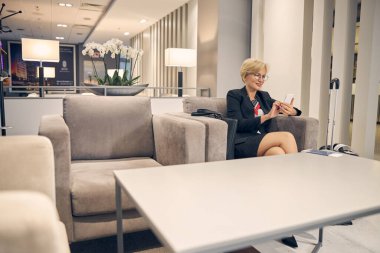 Uçuşunu beklerken akıllı telefon kullanan çekici bir kadın.