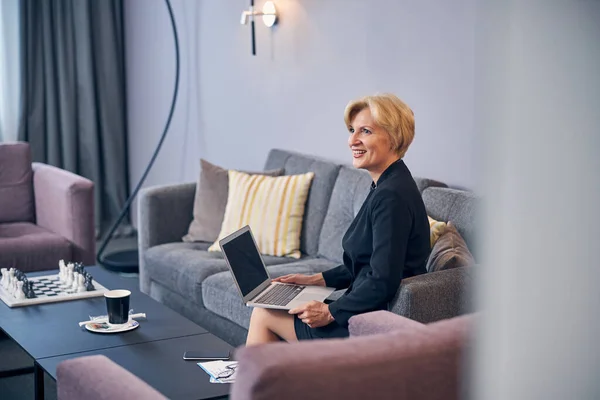 Mujer rubia alegre usando el ordenador portátil en la habitación de hotel —  Fotos de Stock