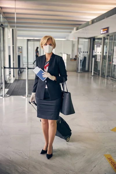 Elegant blond kvinna i medicinsk mask stående på flygplatsen terminal — Stockfoto