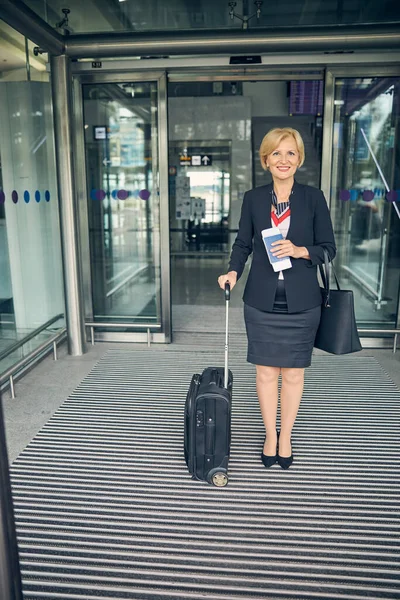 Fröhliche Frau mit Reisekoffer steht im Flughafenterminal — Stockfoto
