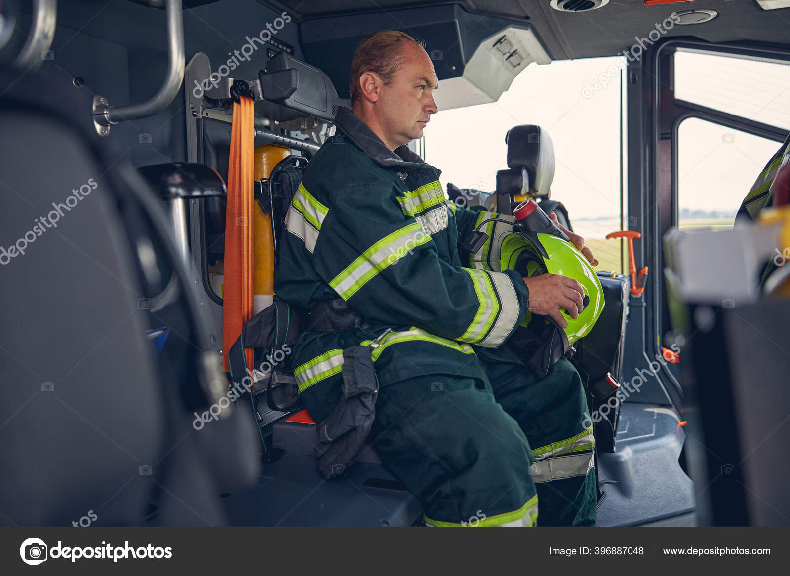 Foto de bombero adulto con casco en las manos sentado en el camión