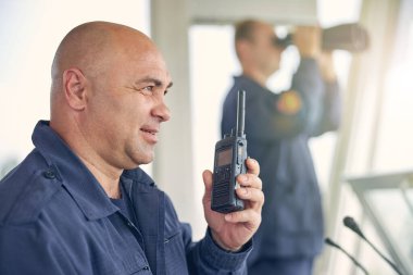 Elinde telsizle gülümseyen yakışıklı işçi.