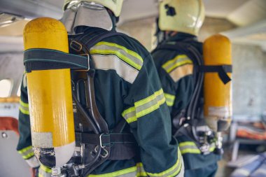 Omuzlarında oksijen tüpü olan iki adam içeride dikiliyor.