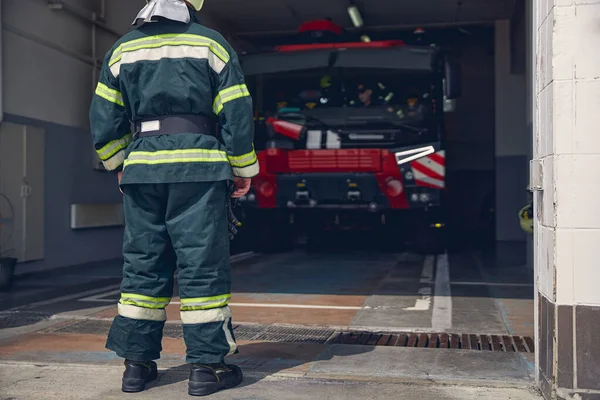 Lång man i skyddande grön uniform stående vid brandstationen — Stockfoto